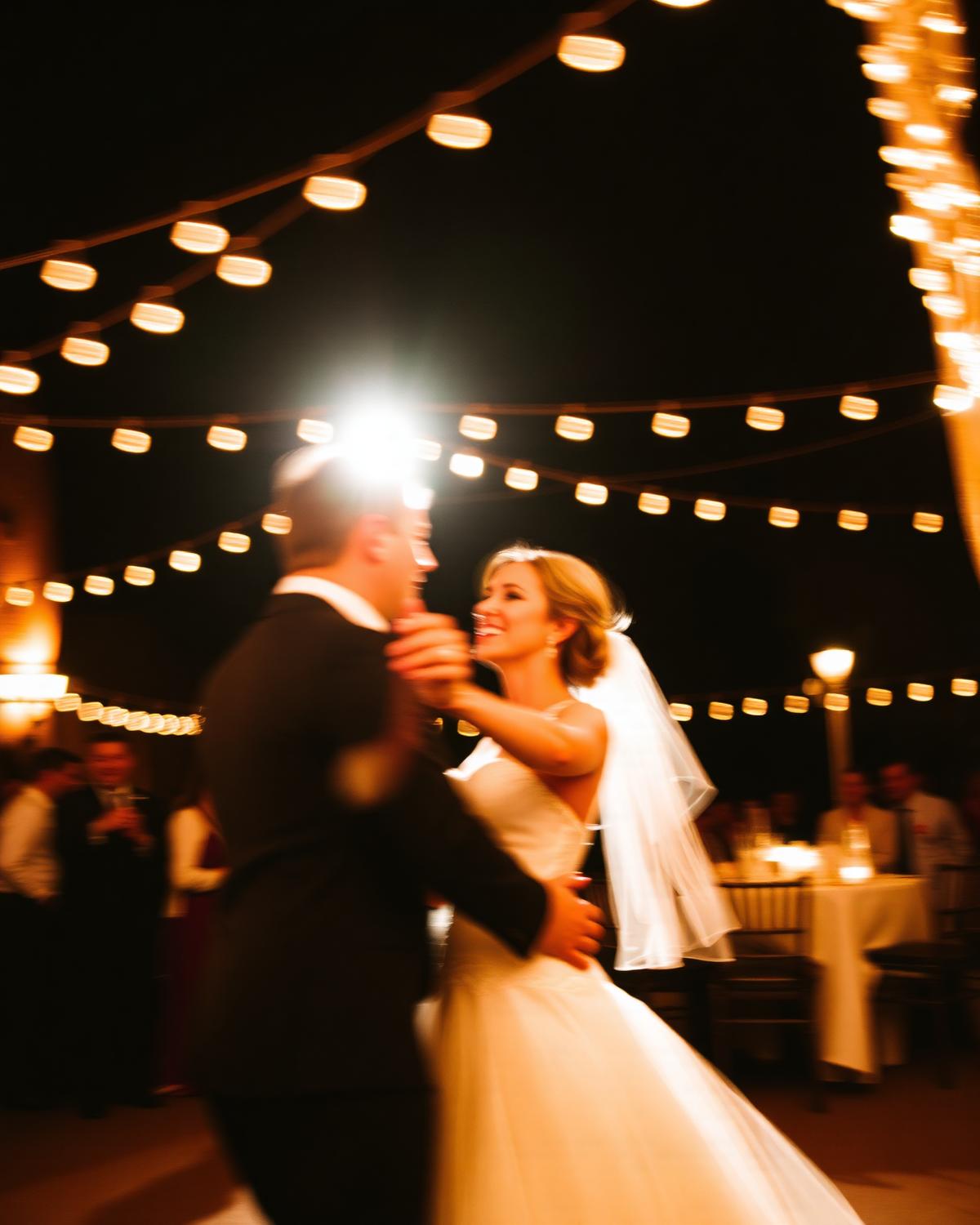 Bride and groom dancing under warm string lights